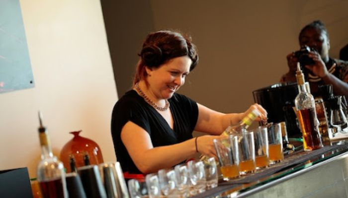 Wineglass stands on bar and woman bartender holds mixing cup and