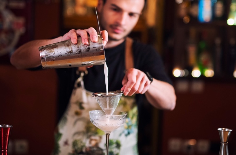 A bartender pouring cocktail in a glass